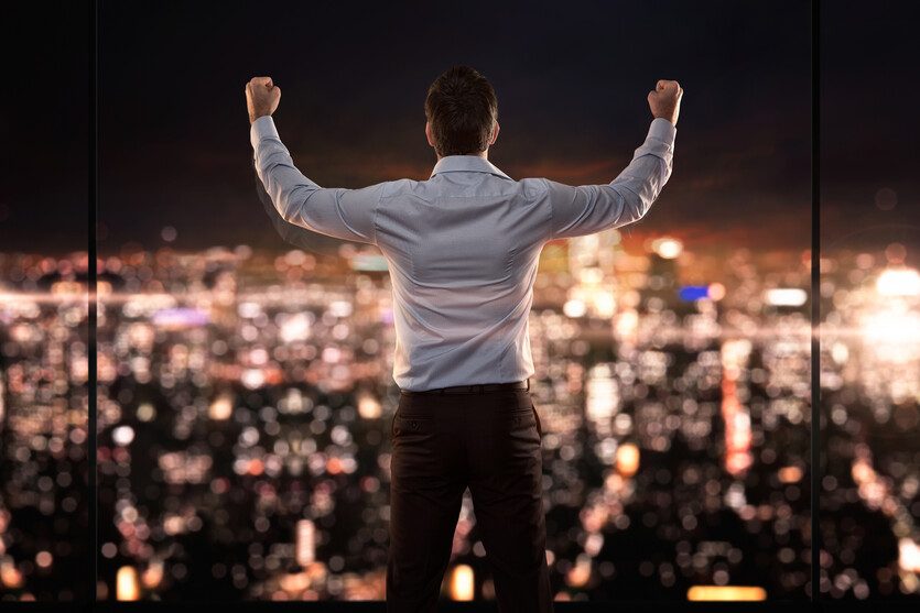Young successful businessman standing in front of the city with his arms raised